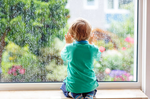 A child sitting and looking out of a window while it rains